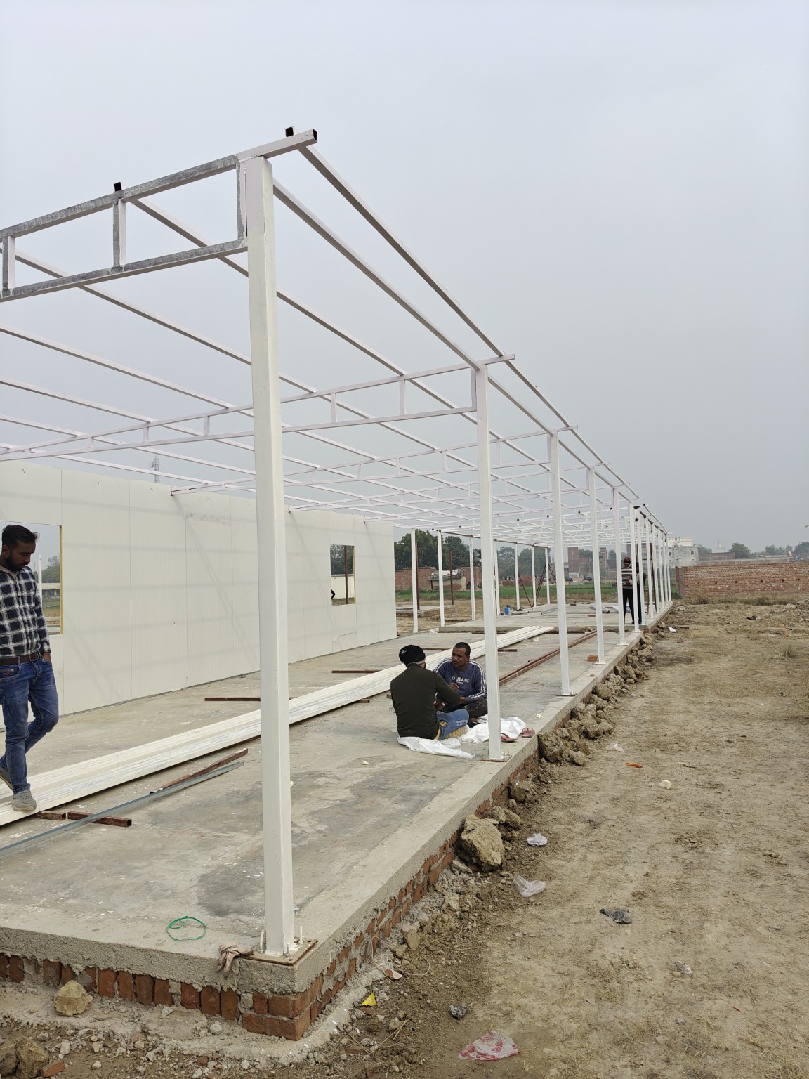 Steel posts, roof members and wall-panel installation along a prefabricated structure.